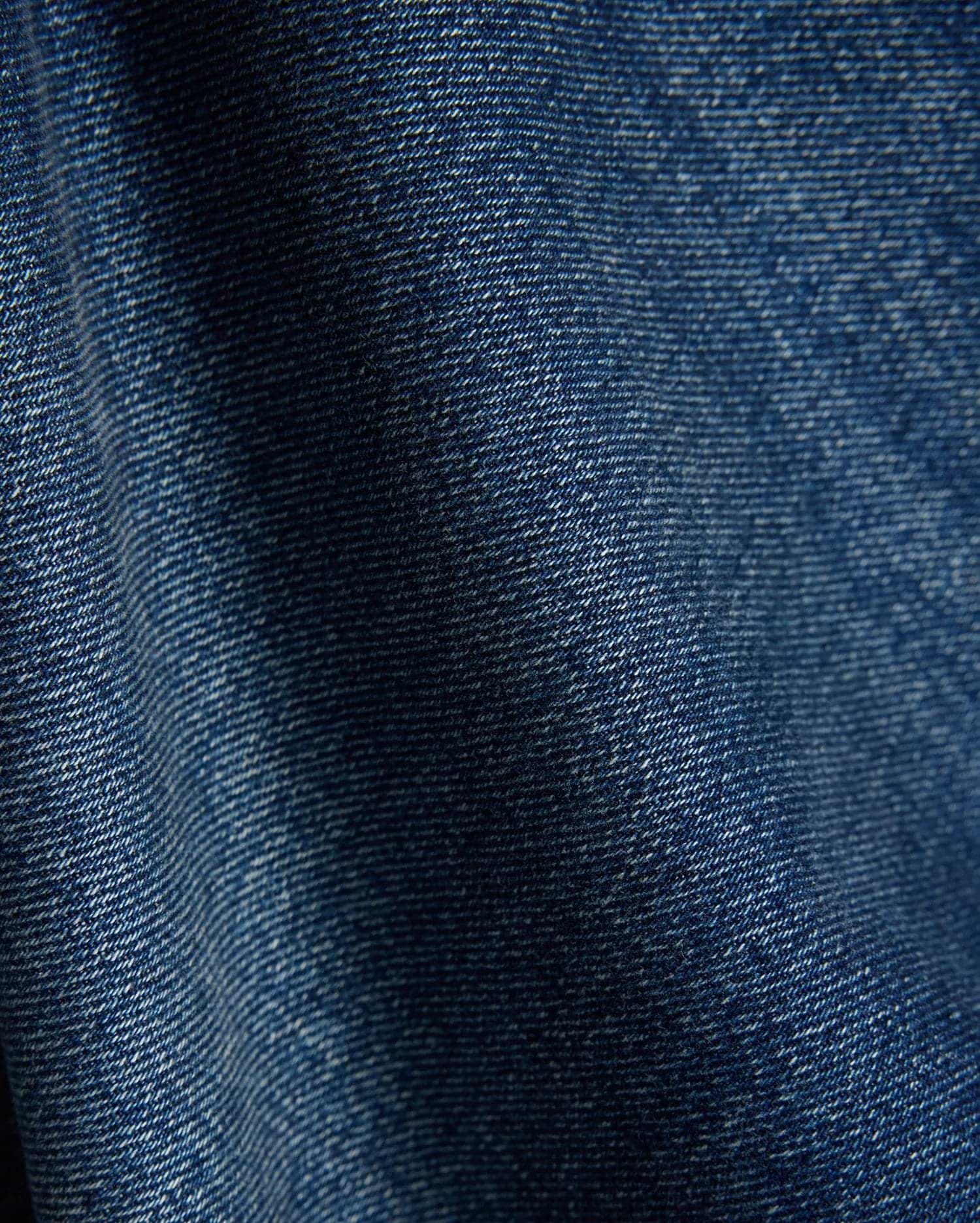 Mens Beck Denim Relaxed Pant in a rich, medium blue wash, showcasing a durable twill weave with subtle white thread accents and natural folds, creating a comfortable, lived-in texture.