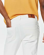 Mustard yellow classic fit pique polo and white slim fit Mens Emerson Denim Pant featuring a brown leather Psycho Bunny skull logo patch on the back waistband.