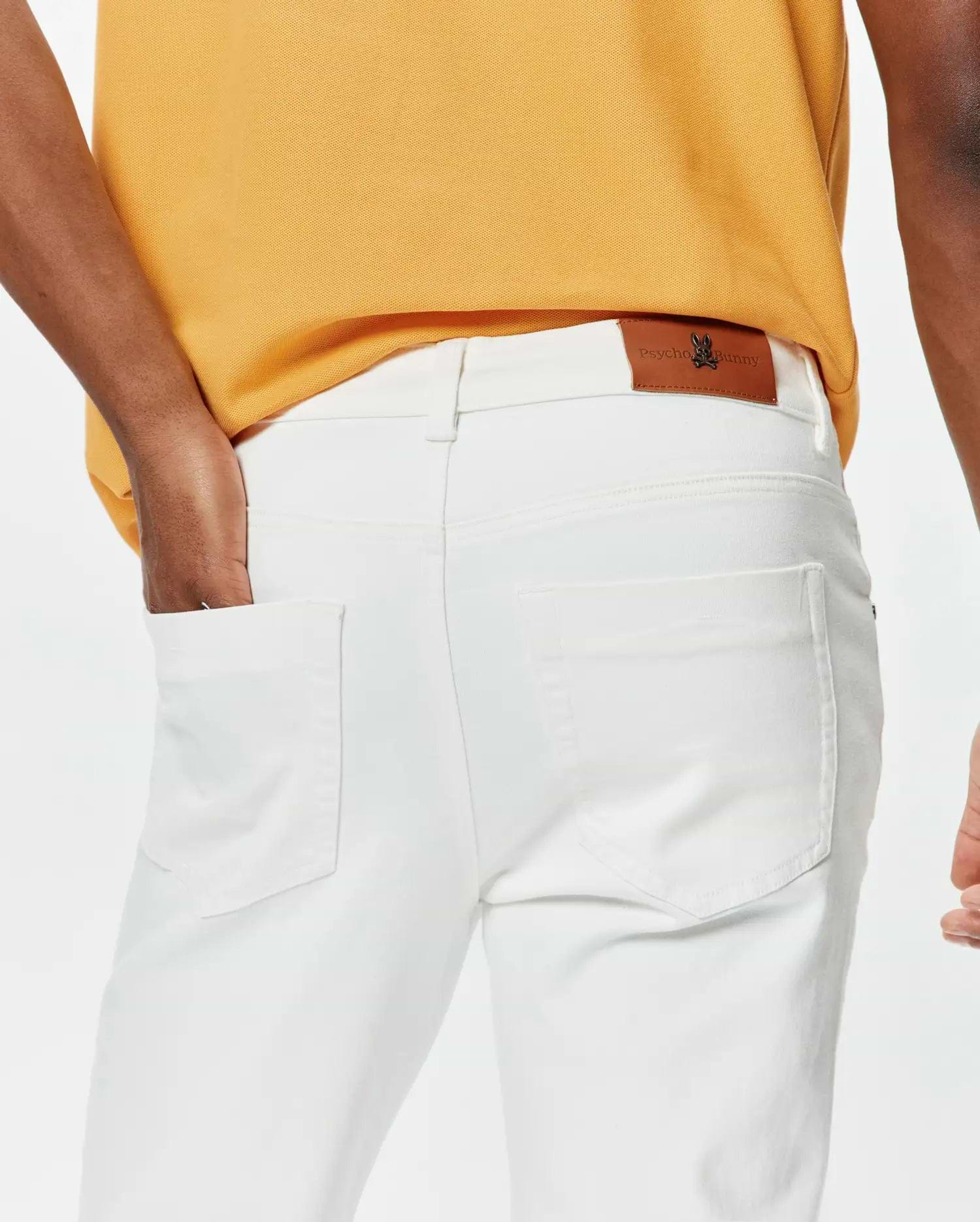 Mustard yellow classic fit pique polo and white slim fit Mens Emerson Denim Pant featuring a brown leather Psycho Bunny skull logo patch on the back waistband.