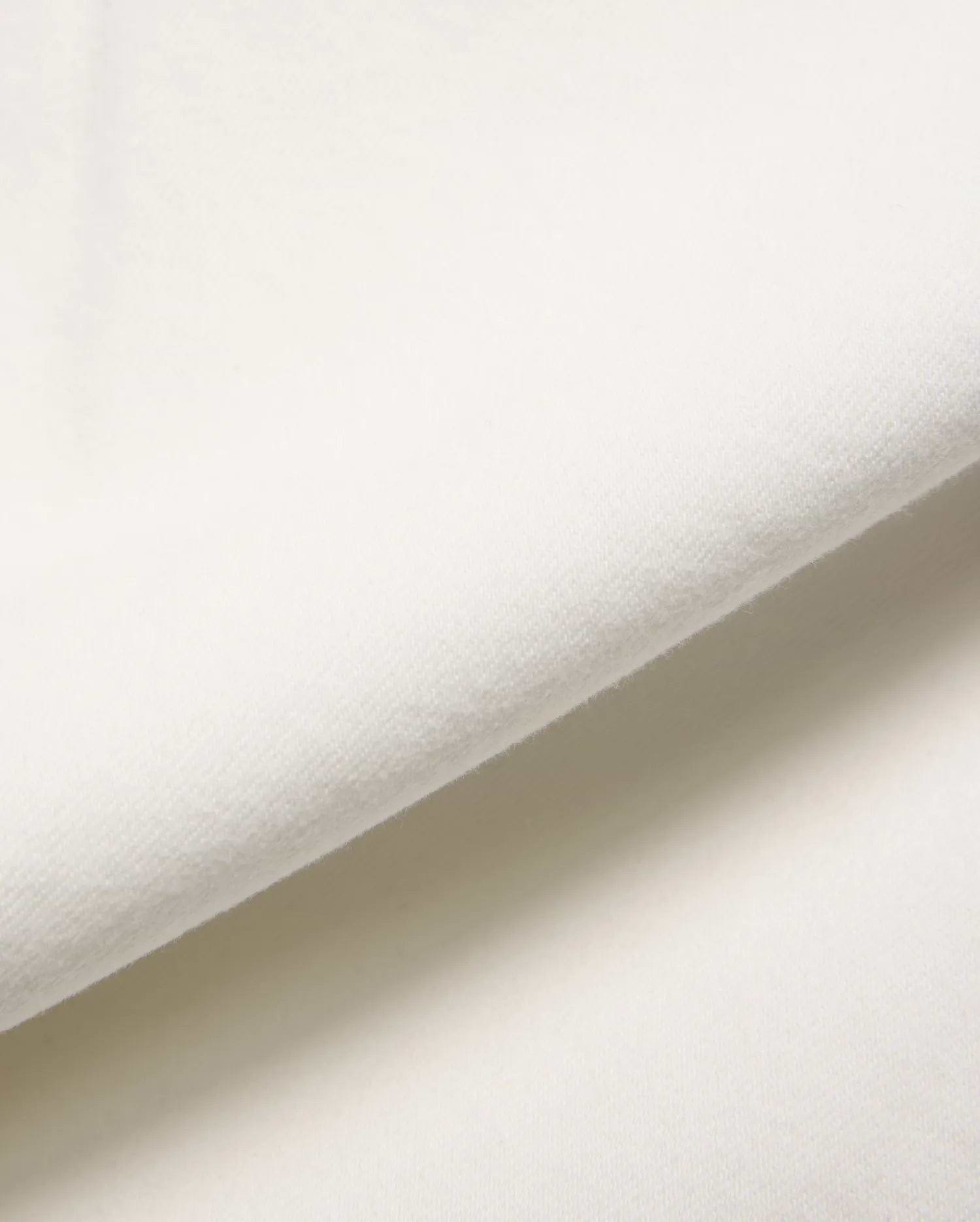 Mens Emerson Denim Pant in a crisp, creamy white, showcasing a premium, soft-touch denim fabric with a subtle, refined twill weave, gently folded to reveal its luxurious texture.