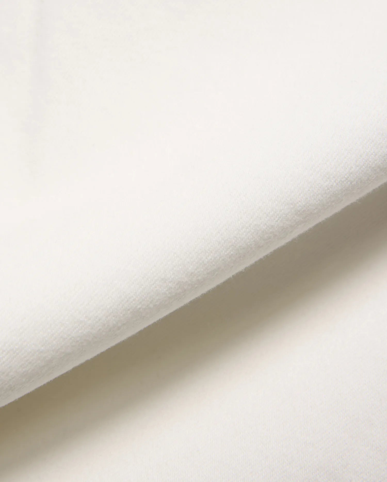 Mens Emerson Denim Pant in a crisp, creamy white, showcasing a premium, soft-touch denim fabric with a subtle, refined twill weave, gently folded to reveal its luxurious texture.