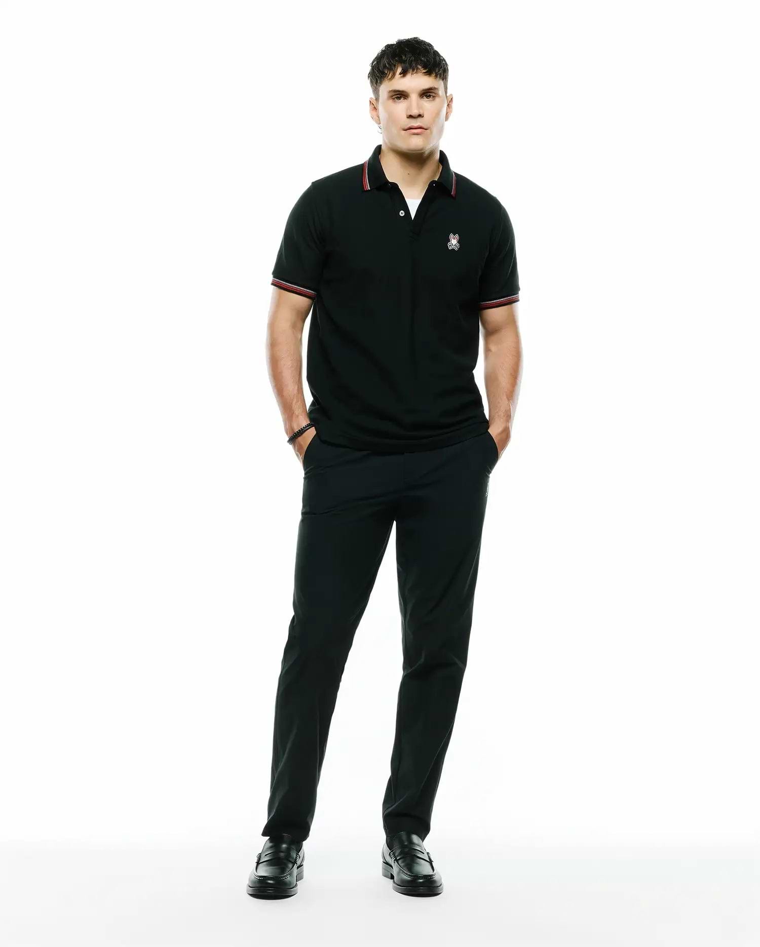 Black pique polo with red and white striped collar and cuffs, featuring an embroidered Psycho Bunny skull logo on the left chest, paired with black Mens Edward 10k Tapered Pant.