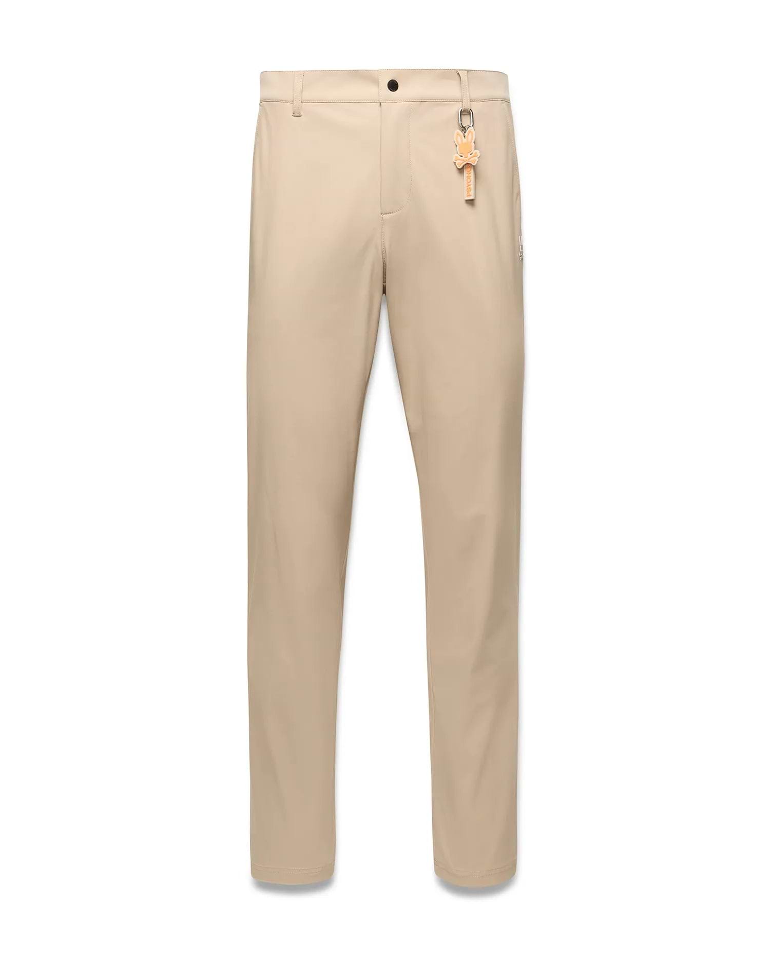 Mens Edward 10k Tapered Pant in beige, crafted from smooth performance fabric with a tapered fit, highlighted by a vibrant orange Psycho Bunny skull keychain on the front belt loop.
