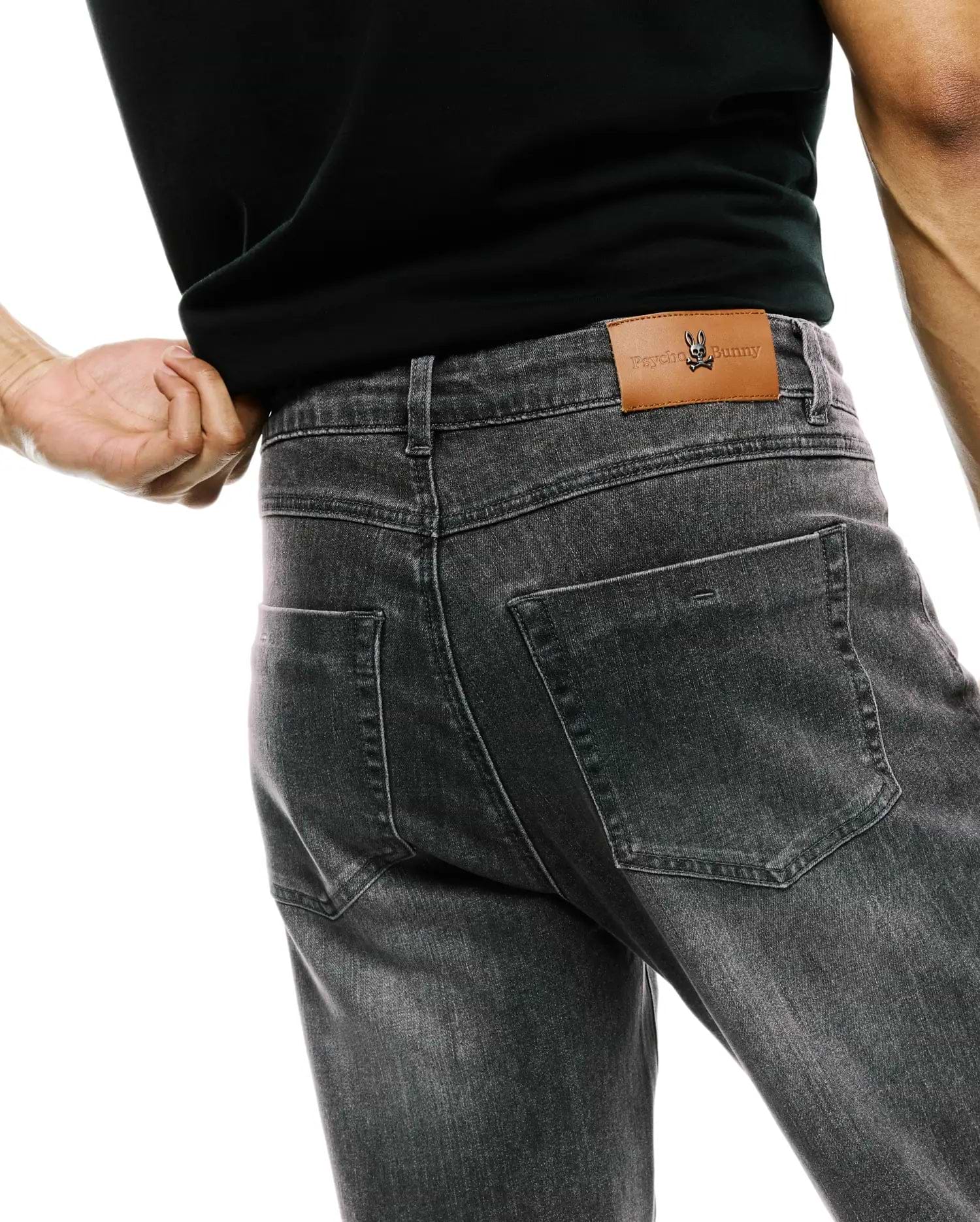 Mens Emerson Denim Pant in washed black, featuring a classic fit, faded denim texture, and a brown leather back waistband patch with an embossed Psycho Bunny logo.