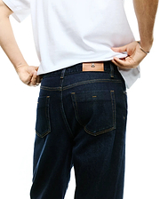 Men's Beck Oversized Denim Pants in dark indigo denim, featuring tan contrast stitching, classic back pockets, and a brown leather Psycho Bunny skull logo patch on the rear waistband. (2)