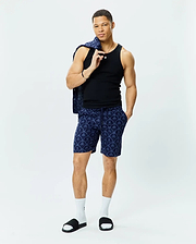 Black slim-fit ribbed tank top, Mens Brad Linen Short 8 1/2 in navy with a relaxed fit and all-over light blue Psycho Bunny skull and palm tree pattern, paired with a matching patterned button-up shirt.