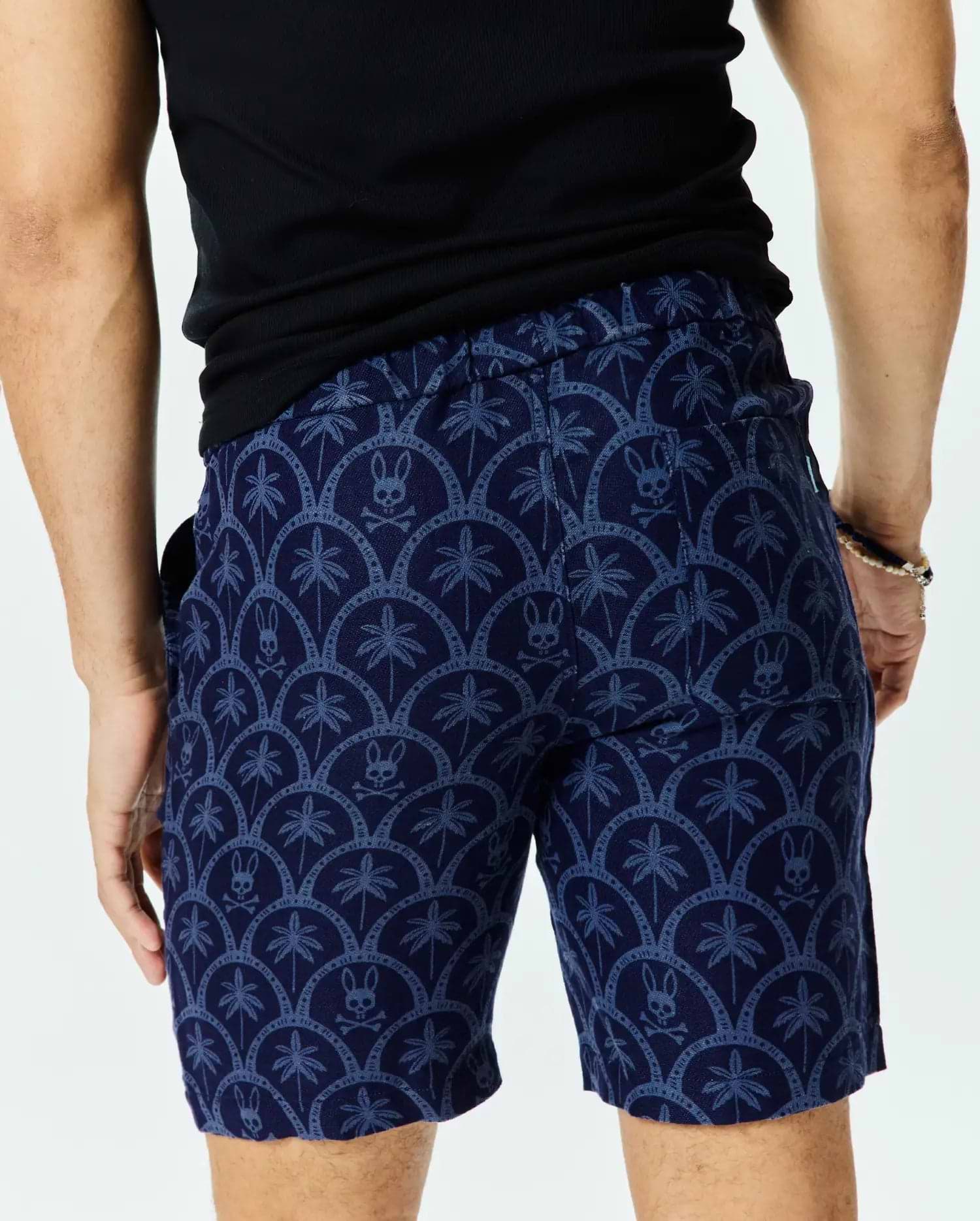 Mens Brad Linen Short 8 1/2, navy blue with a light blue all-over pattern of palm trees and Psycho Bunny skull logos in a scalloped design, classic fit linen blend.
