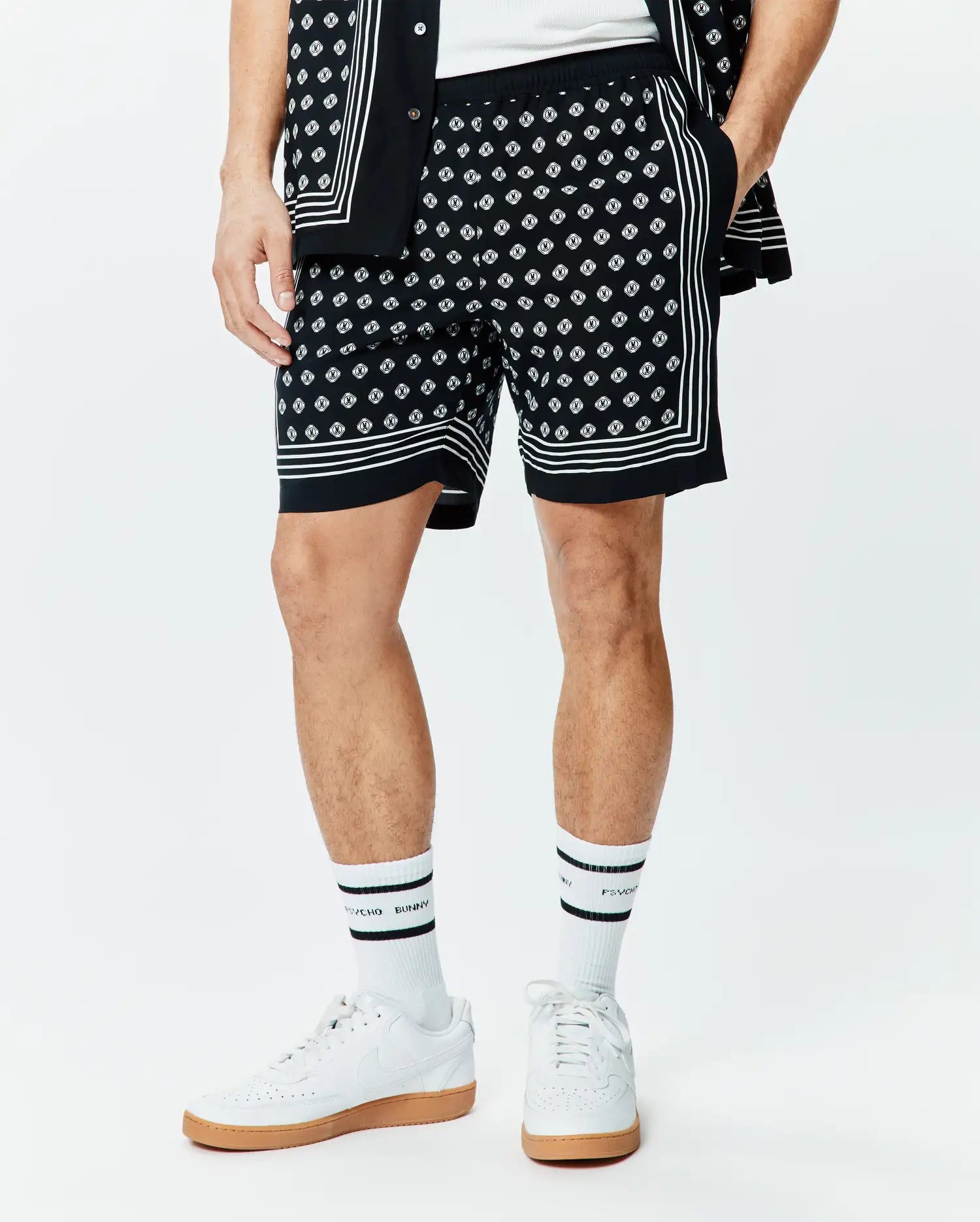 Mens Nick Tencel Short 7, black with an all-over white Psycho Bunny skull logo pattern, featuring white border stripes on the sides and hem, in a relaxed fit smooth Tencel fabric.
