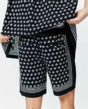 Mens Nick Tencel Short 7 in black, featuring a relaxed fit and smooth Tencel fabric. It has an all-over white Psycho Bunny skull logo diamond print, accented with bold white triple stripes along the side seams and hem.