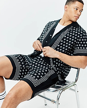 Black short-sleeve shirt and Mens Nick Tencel Short 7 with an all-over white Psycho Bunny skull logo pattern. White stripe accents on placket, cuffs, and shorts hem provide a relaxed fit.