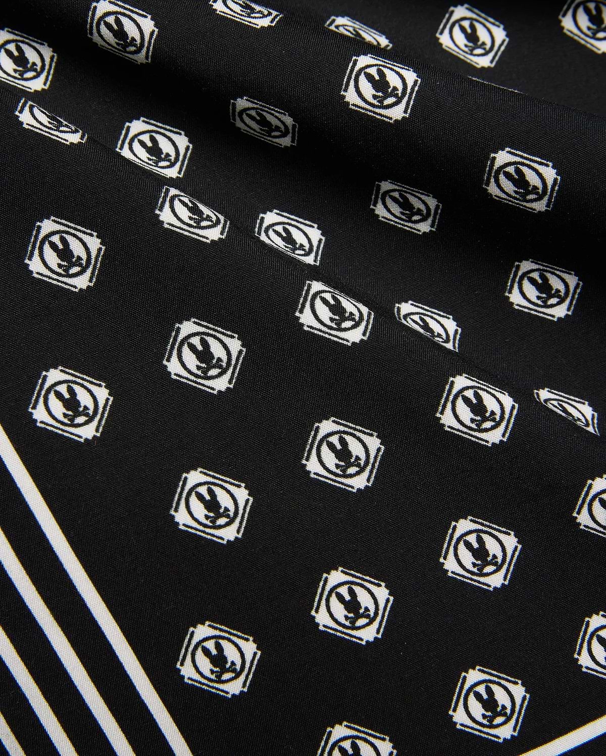 Mens Nick Tencel Short 7, black fabric with all-over white Psycho Bunny skull logo pattern in square frames, featuring bold white diagonal stripes. Smooth Tencel texture.