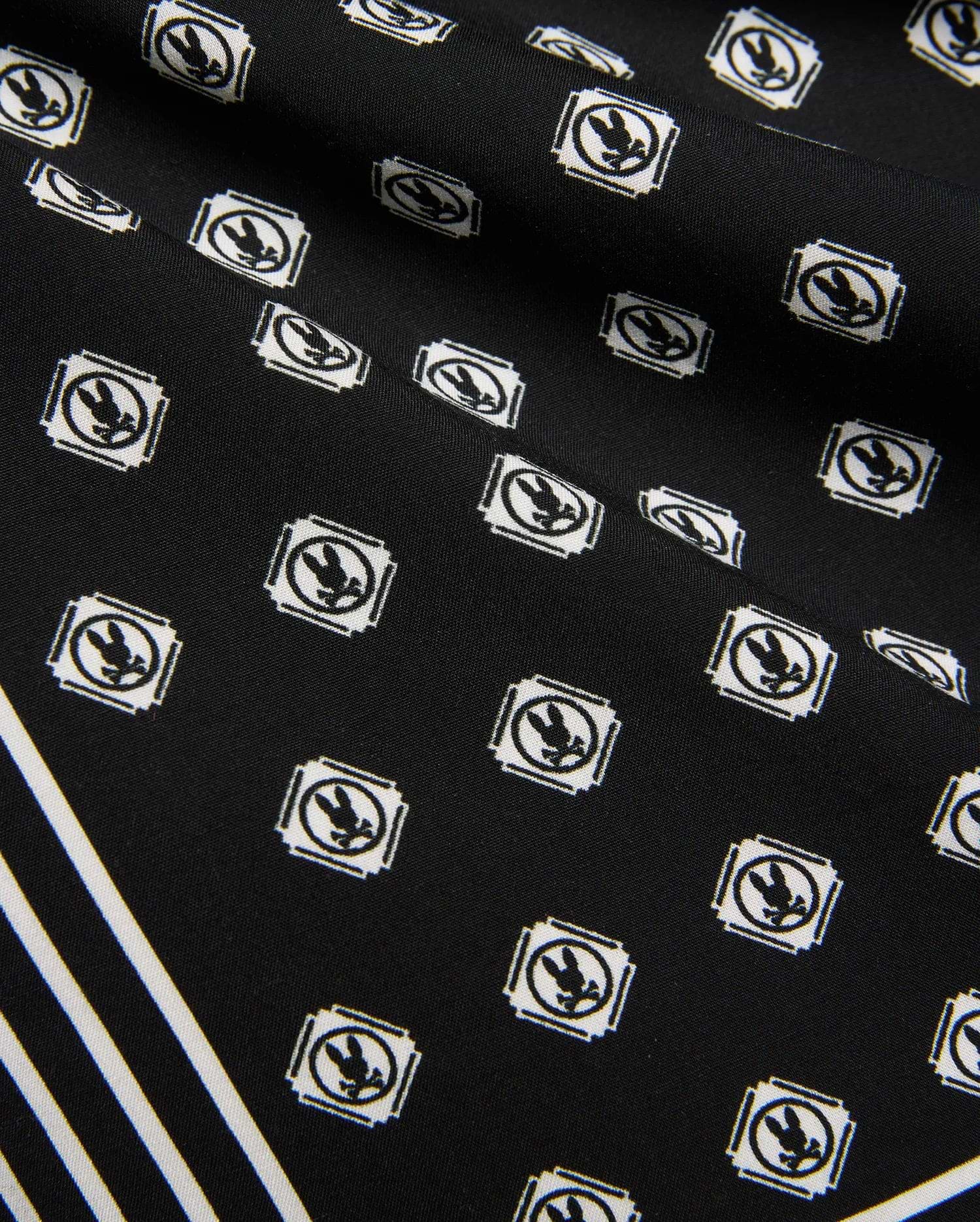 Mens Nick Tencel Short 7, black fabric with all-over white Psycho Bunny skull logo pattern in square frames, featuring bold white diagonal stripes. Smooth Tencel texture.