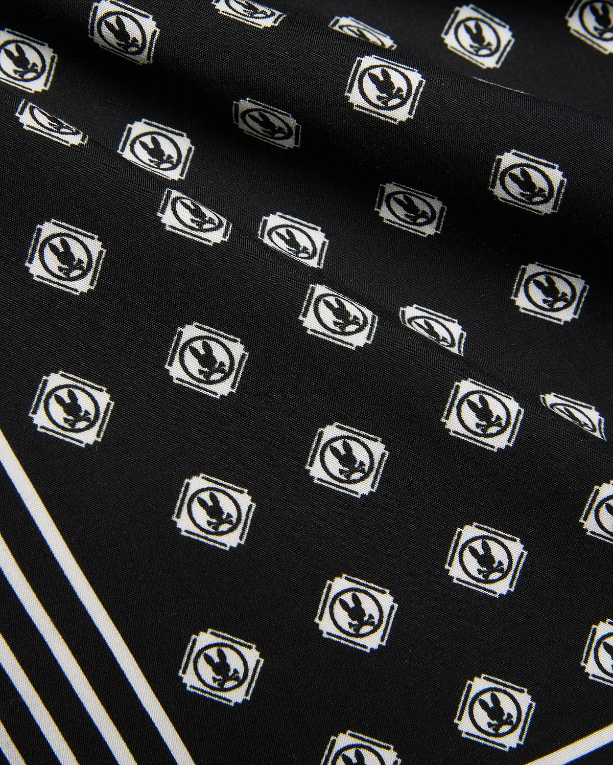 Mens Nick Tencel Short 7, black fabric with all-over white Psycho Bunny skull logo pattern in square frames, featuring bold white diagonal stripes. Smooth Tencel texture.