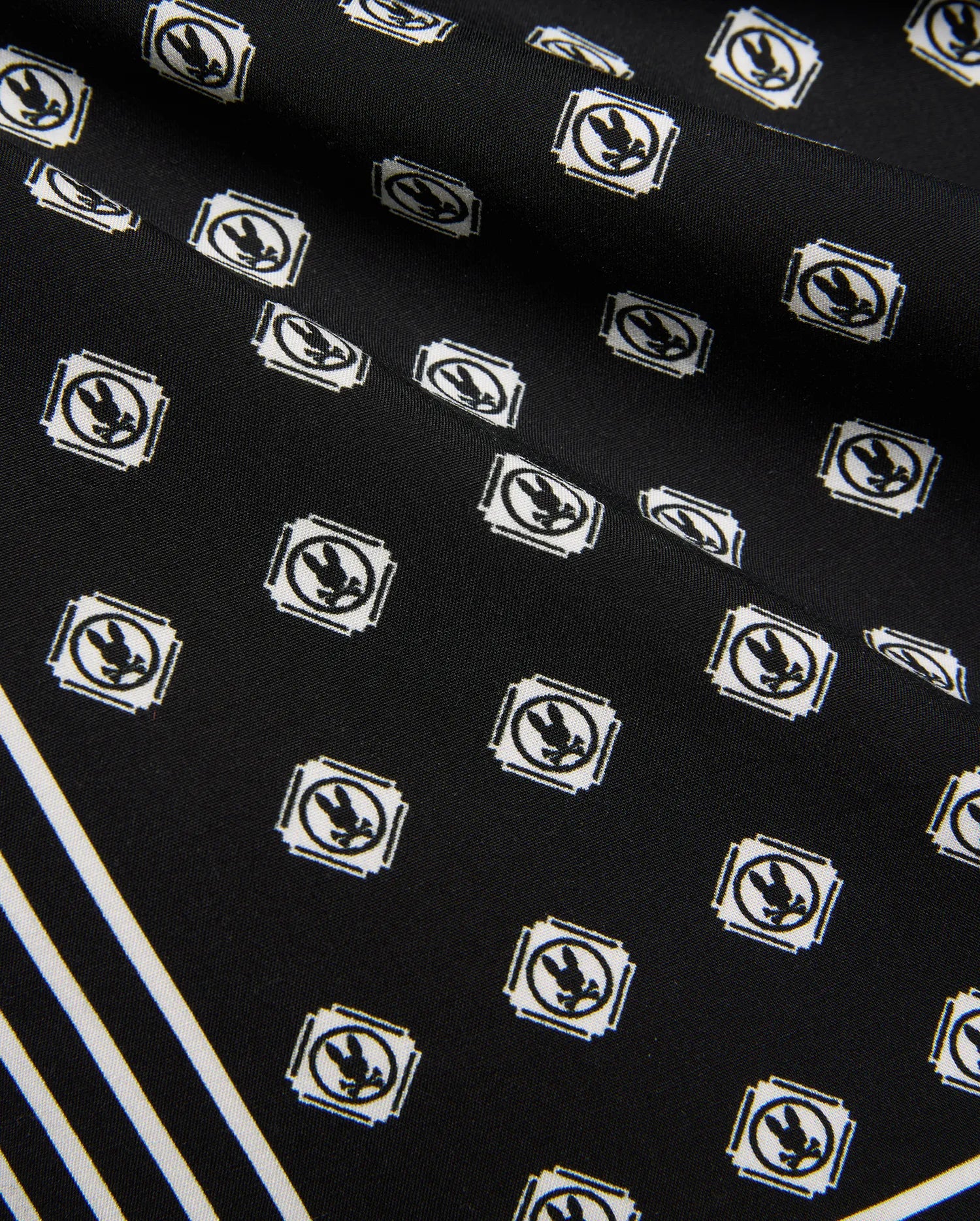 Mens Nick Tencel Short 7, black fabric with all-over white Psycho Bunny skull logo pattern in square frames, featuring bold white diagonal stripes. Smooth Tencel texture.