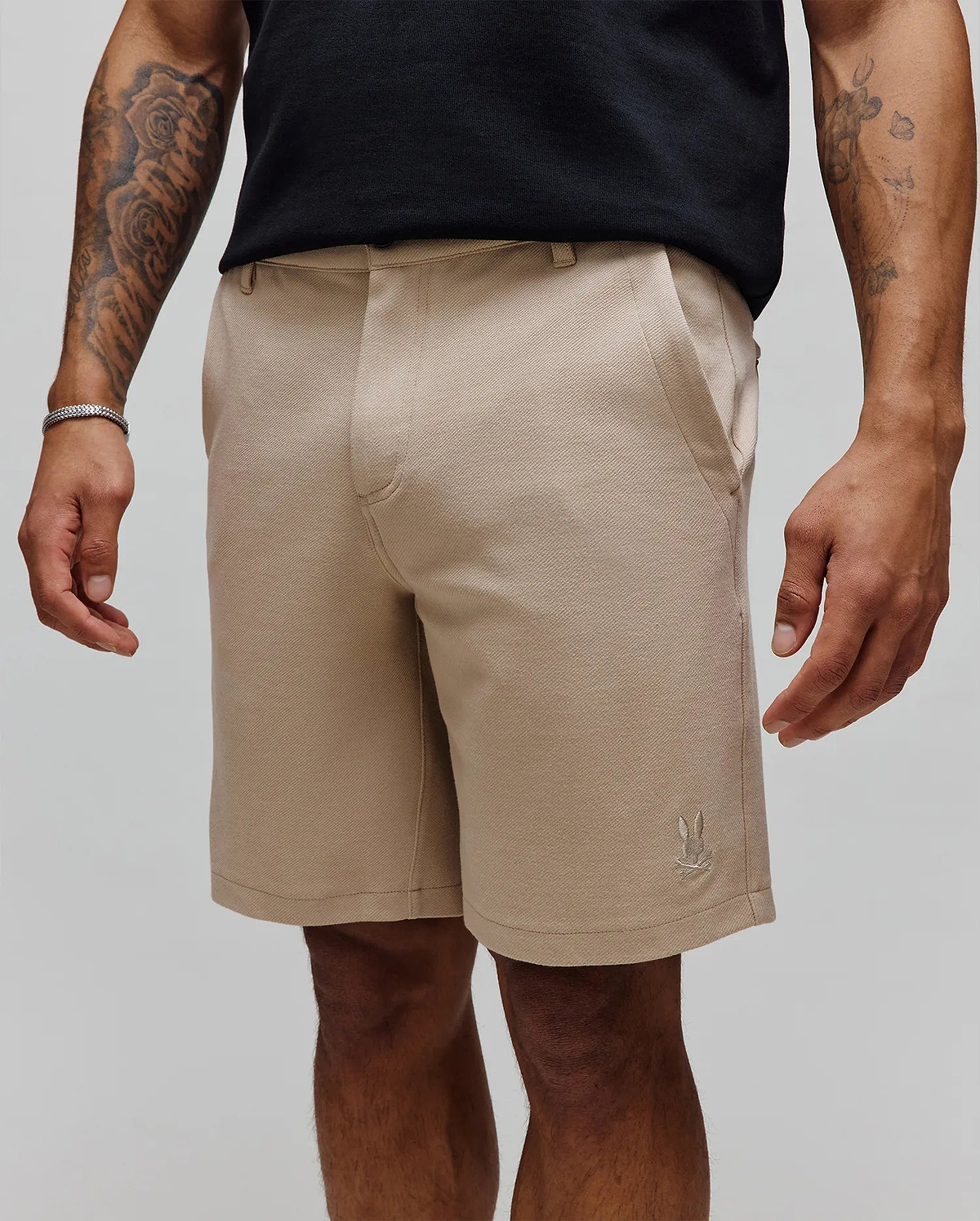 Mens Shiro Twill Short in classic fit beige twill fabric, featuring a subtle diagonal weave and a small, embroidered Psycho Bunny skull logo on the lower left leg.