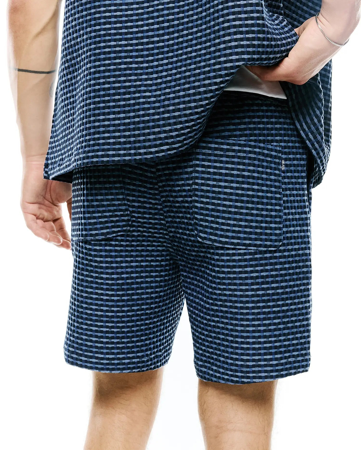 Mens Erik Raised Check Short, blue and dark blue relaxed fit shorts with a raised check texture, featuring two back patch pockets and a small white embroidered Psycho Bunny skull logo on the right pocket.