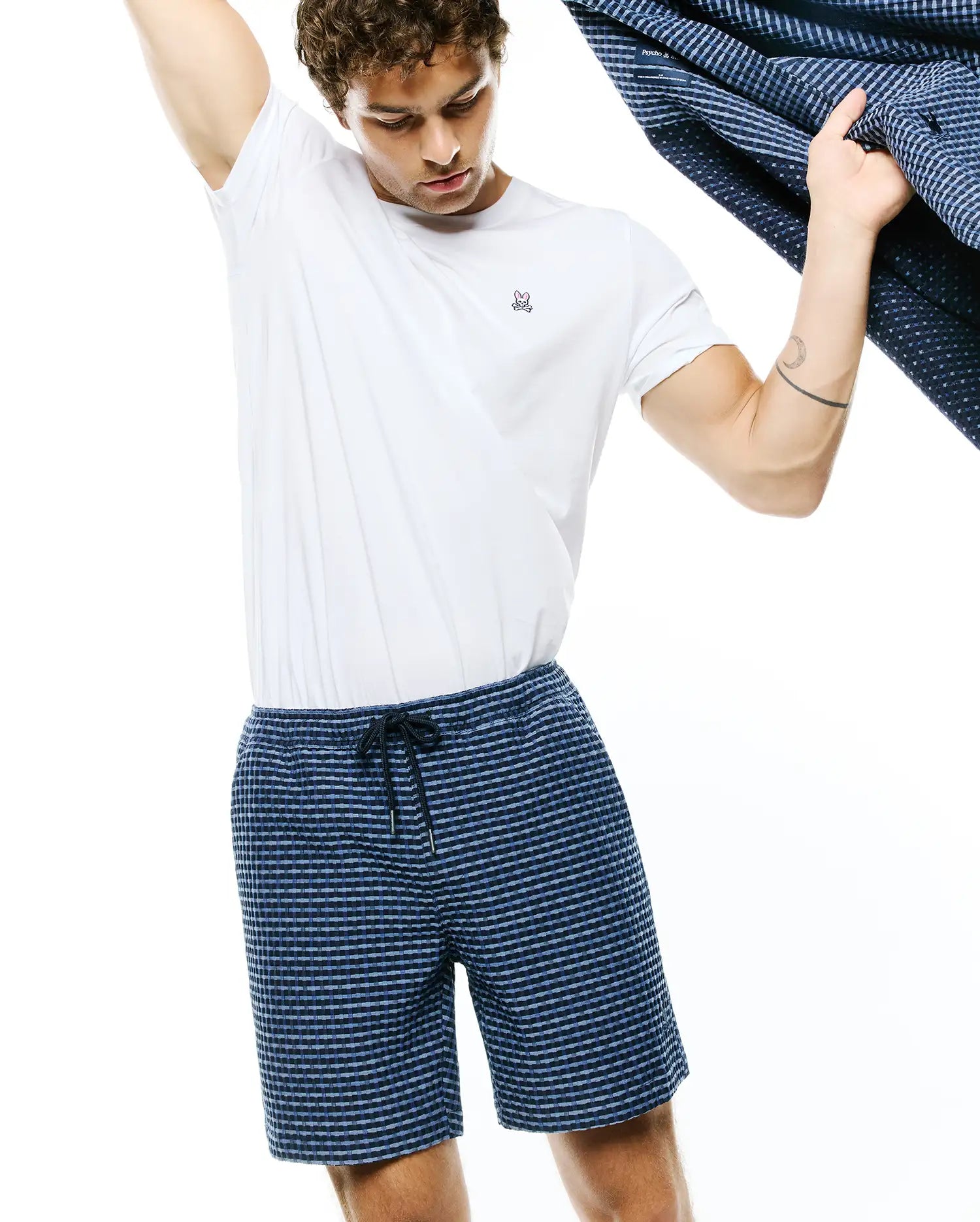 White jersey t-shirt with small embroidered Psycho Bunny skull logo on left chest, paired with Mens Erik Raised Check Short in navy and light blue, featuring a textured pattern and drawstring waist.