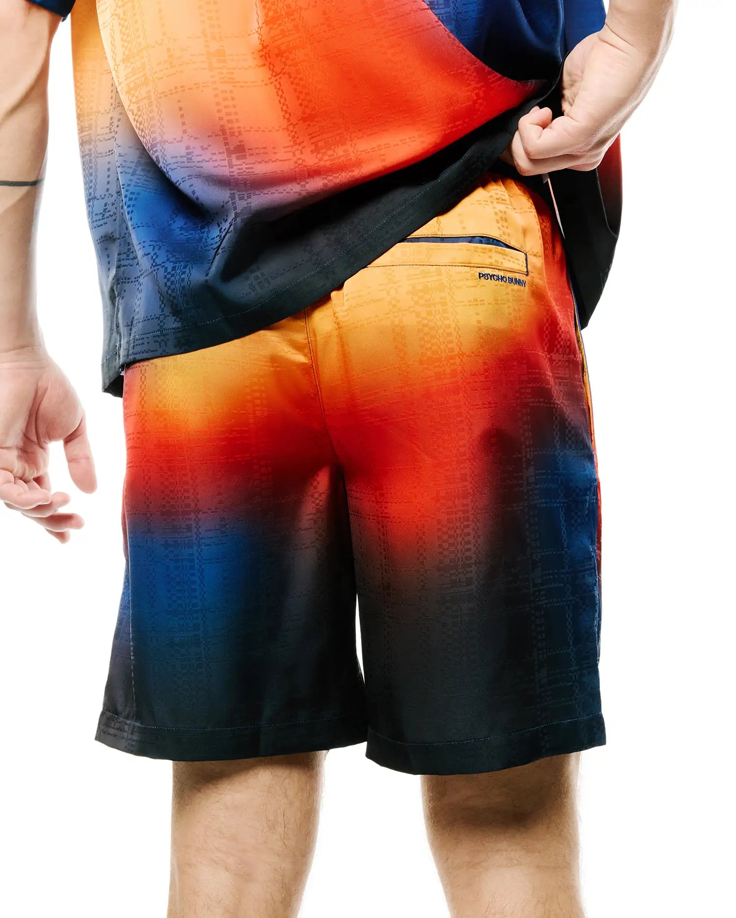 Mens Zander Jacquard Short, a relaxed fit short with a vibrant orange-red to deep blue gradient, featuring a subtle geometric jacquard pattern and a small Psycho Bunny text logo on the back right pocket.