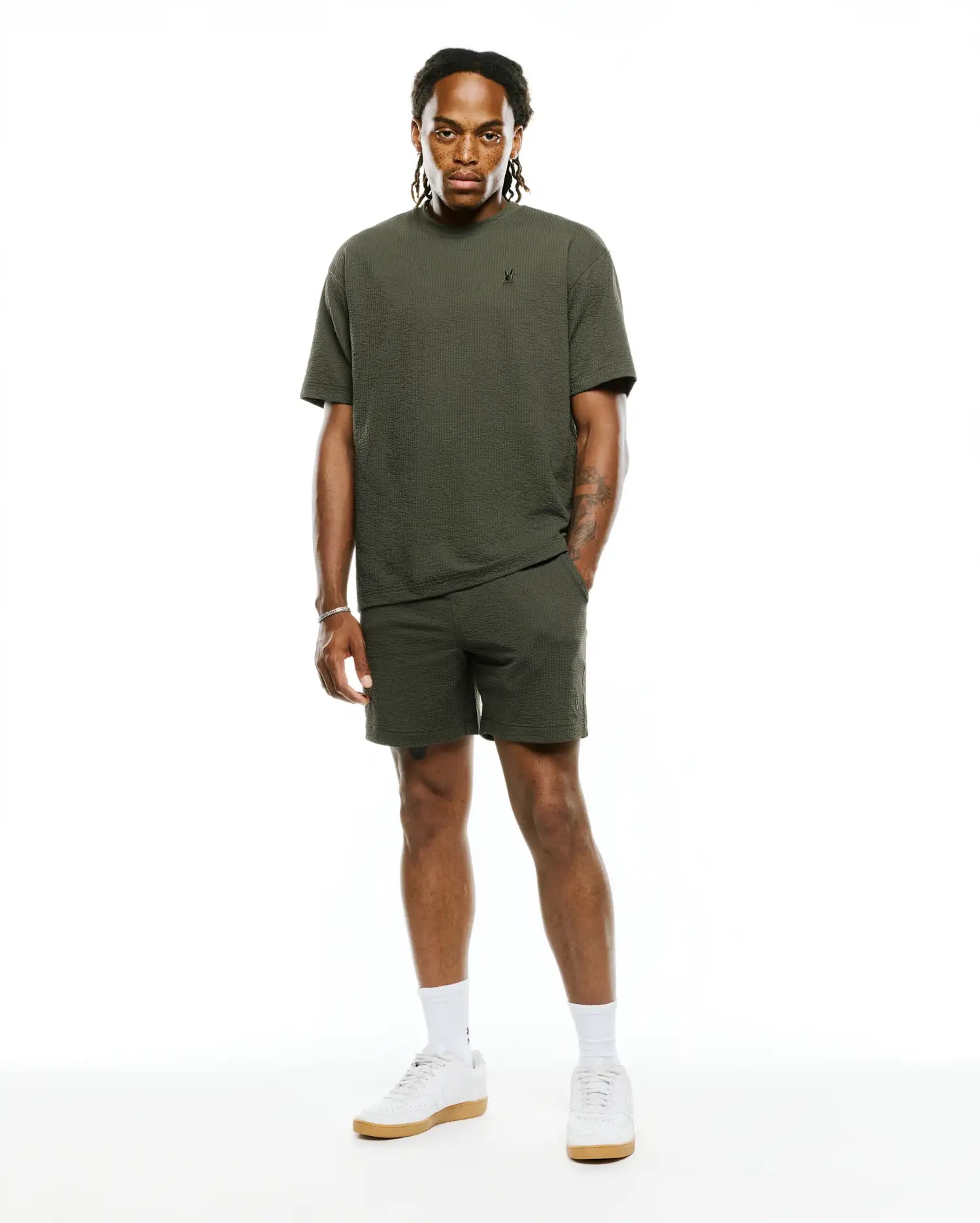 Relaxed fit olive green Mens Arlen Seersucker Short and matching textured T-shirt, both featuring small embroidered black Psycho Bunny skull logos on the left thigh and chest. (4)
