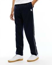 Harland Double Weave Chalk Stripe Track Pant in navy with white pinstripes, featuring a white and light green side stripe and a small embroidered white Psycho Bunny skull logo on the left thigh, classic fit. (2)