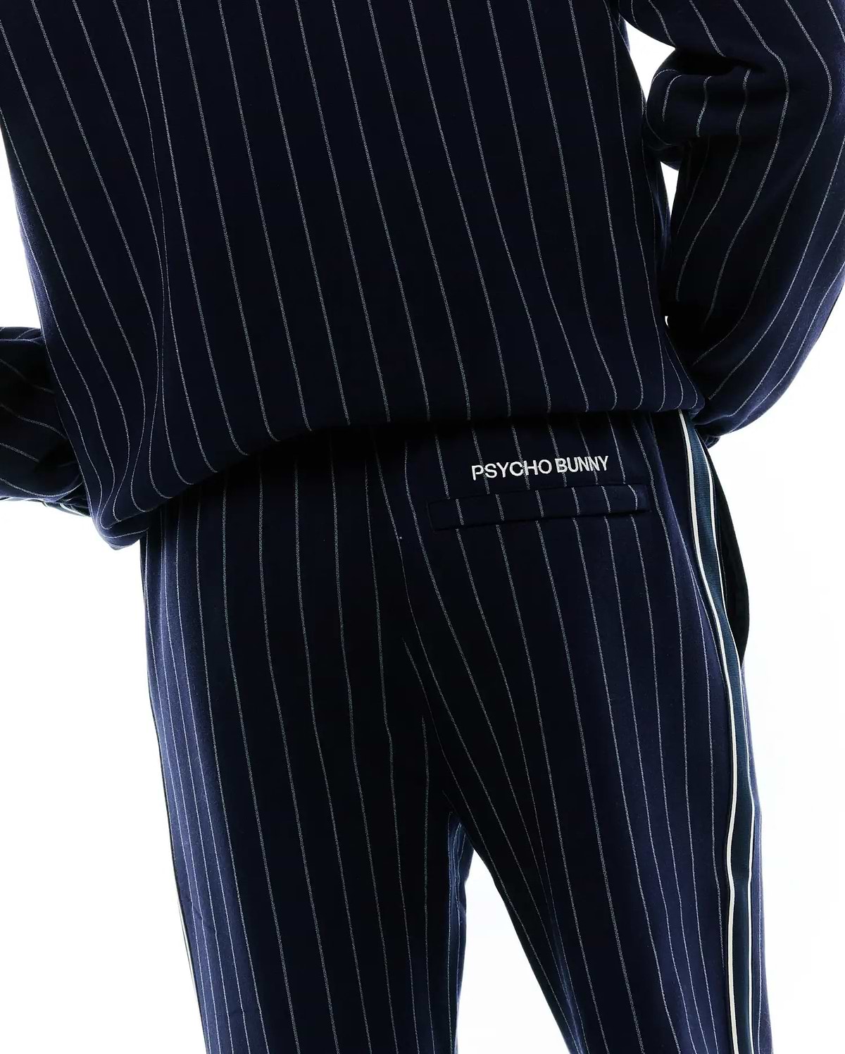 Mens Harland Double Weave Chalk Stripe Track Pant, navy with fine white pinstripes, a relaxed fit, and a prominent white side stripe. White embroidered PSYCHO BUNNY branding is on the back flap pocket. (4)