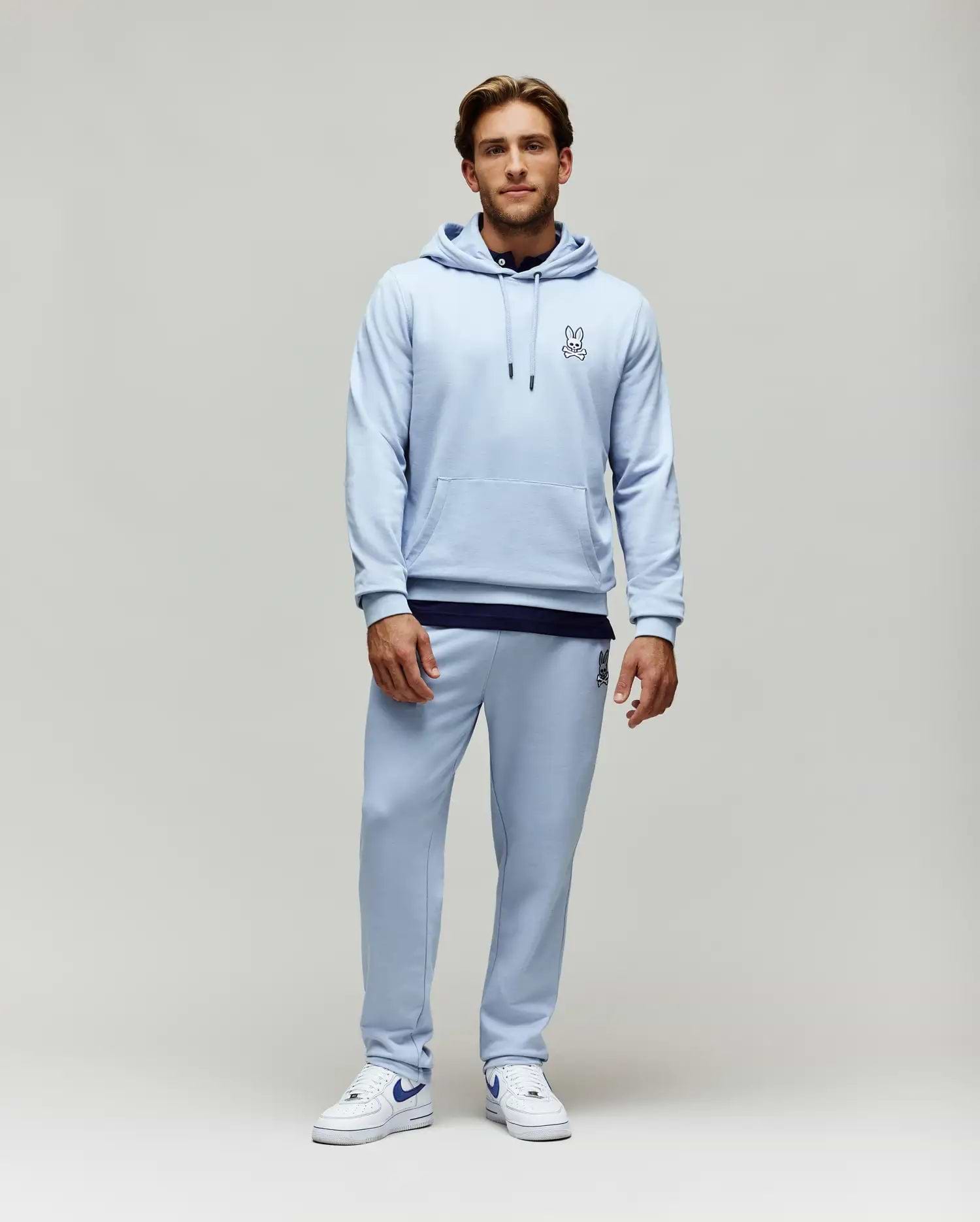 Light blue relaxed fit French terry hoodie with small embroidered Psycho Bunny skull logo on chest, kangaroo pocket, and matching Mens Timothy 4k Bunny Jogger with larger embroidered logo on thigh.