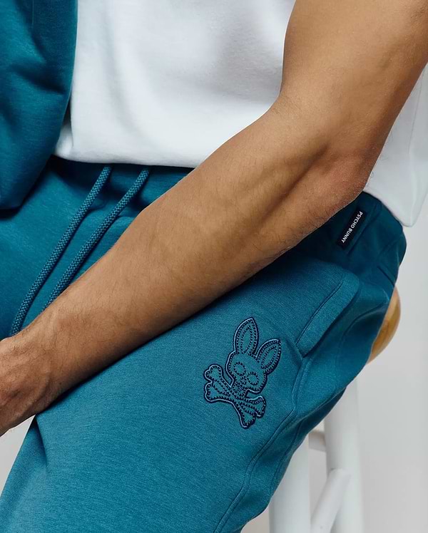 Mens Barry Joggers in deep teal french terry, featuring a relaxed fit, black drawstring, and a medium-sized black embroidered Psycho Bunny skull logo on the left thigh, plus a Psycho Bunny tag on the waistband.