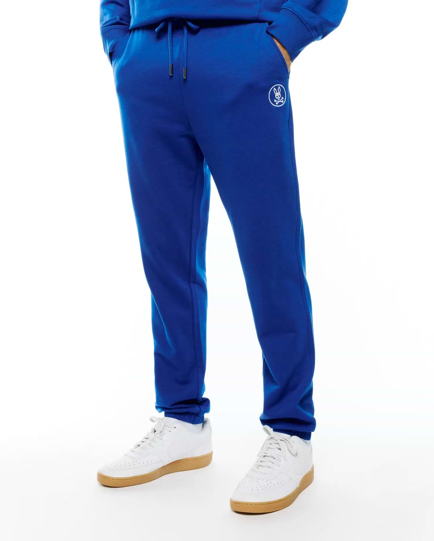 Mens Nathaniel Sweatpant, royal blue French terry with a relaxed tapered fit, featuring a drawstring waist with silver tips, ribbed cuffs, and a small white embroidered Psycho Bunny skull logo on the left thigh.