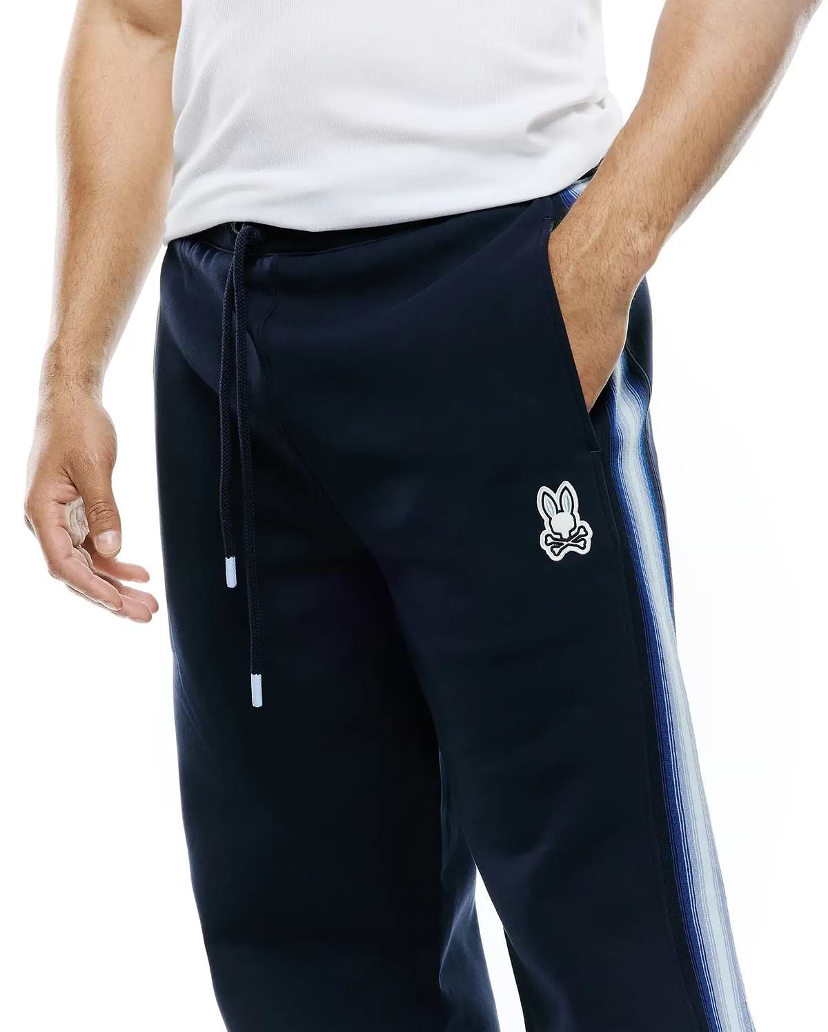 Mens Jaydon Track Pant in navy, featuring a relaxed fit, smooth knit fabric, drawstring waist, and a small embroidered Psycho Bunny skull logo on the left thigh, with a blue and white striped side panel. (4)