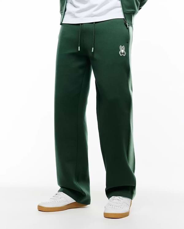 Mens Jaydon Track Pant in dark green, featuring a relaxed wide leg fit, smooth knit fabric, drawstring waist with white tips, and a small embroidered white Psycho Bunny skull logo on the left hip. (3)