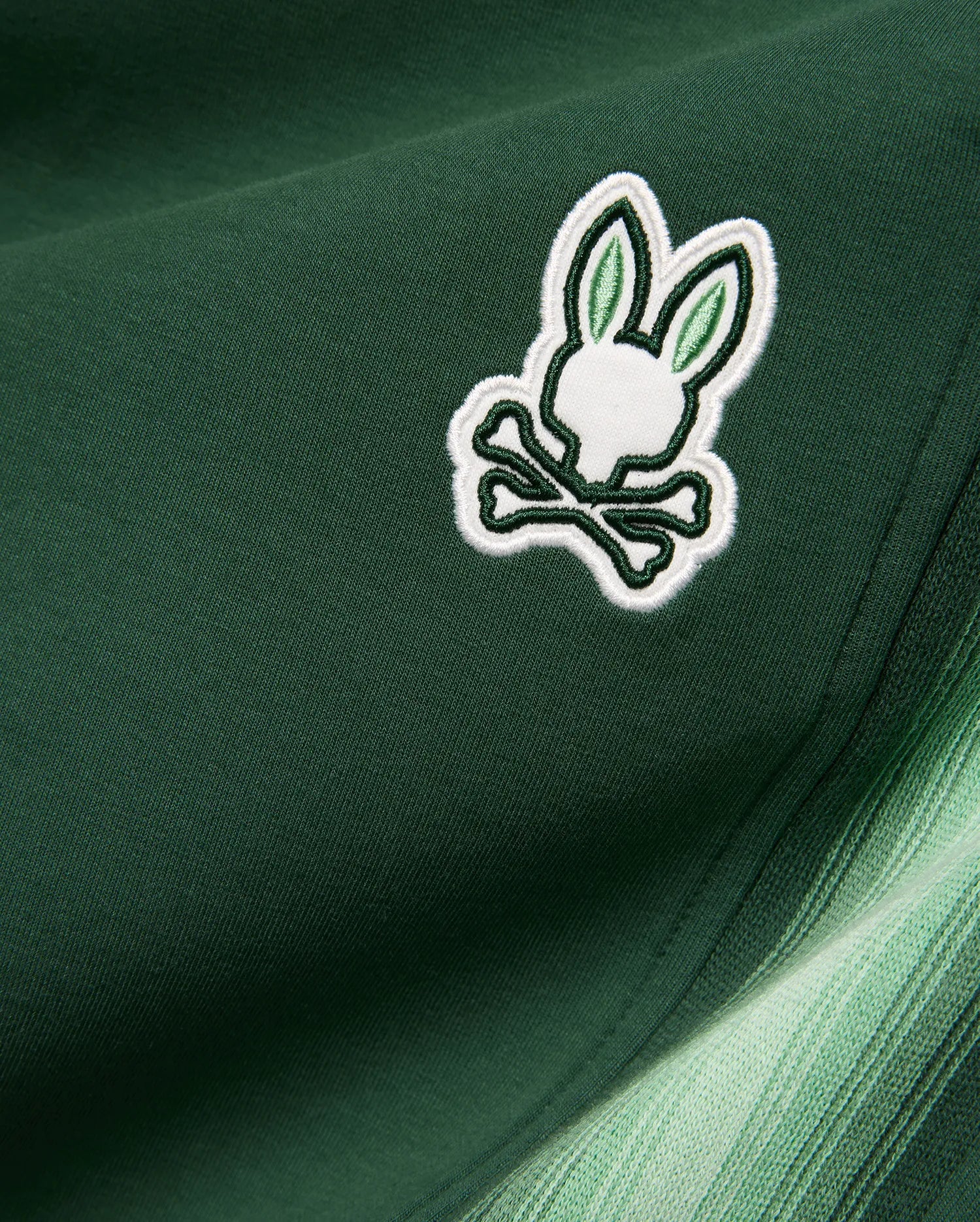 Mens Jaydon Track Pant in dark green smooth knit, featuring a small embroidered white and light green Psycho Bunny skull logo and a side stripe with a green gradient. (6)