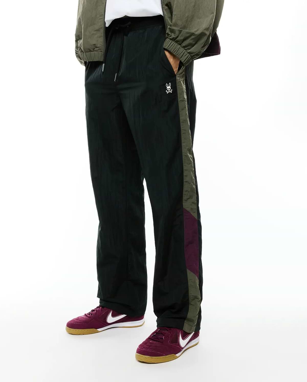 Deep green crinkled nylon Alder Nylon Colorblock Pant with a relaxed fit, featuring olive green and burgundy side stripes and a small white embroidered Psycho Bunny skull logo on the left thigh.