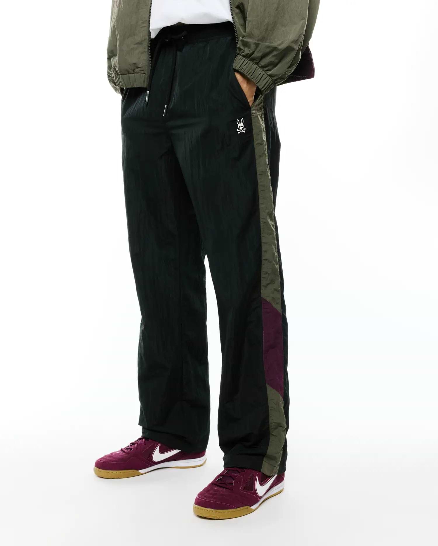 Deep green crinkled nylon Alder Nylon Colorblock Pant with a relaxed fit, featuring olive green and burgundy side stripes and a small white embroidered Psycho Bunny skull logo on the left thigh.