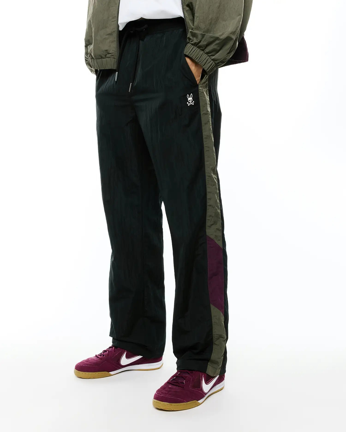 Deep green crinkled nylon Alder Nylon Colorblock Pant with a relaxed fit, featuring olive green and burgundy side stripes and a small white embroidered Psycho Bunny skull logo on the left thigh.