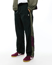 Deep green crinkled nylon Alder Nylon Colorblock Pant with a relaxed fit, featuring olive green and burgundy side stripes and a small white embroidered Psycho Bunny skull logo on the left thigh.