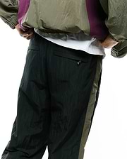 Mens Alder Nylon Colorblock Pant in deep forest green with a relaxed fit, crinkled nylon texture, and a contrasting olive green side stripe. A small zipper pull is visible on the back pocket.