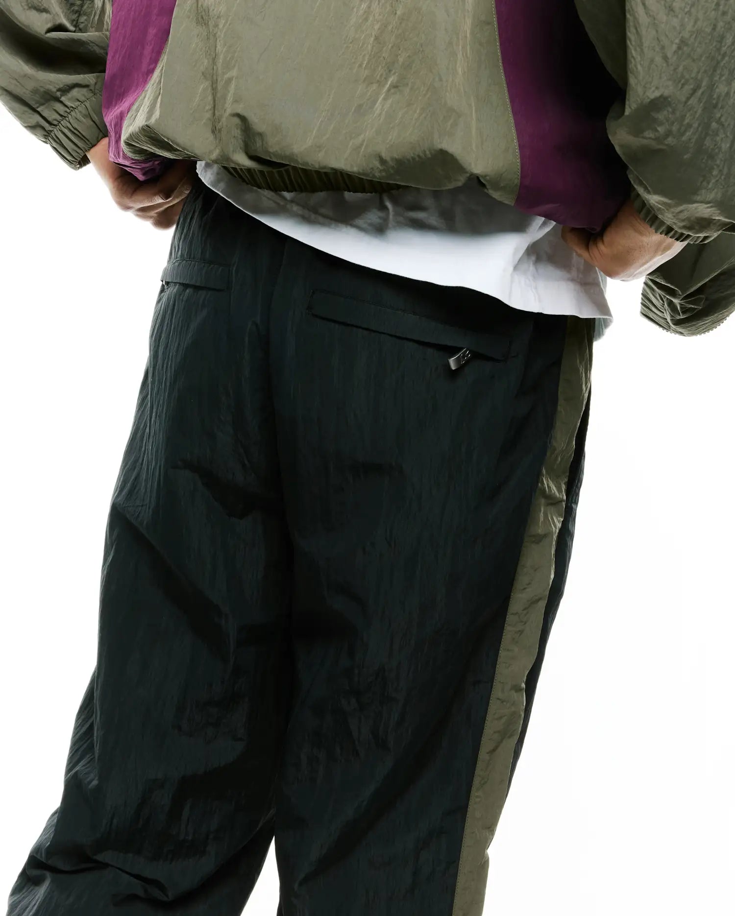 Mens Alder Nylon Colorblock Pant in deep forest green with a relaxed fit, crinkled nylon texture, and a contrasting olive green side stripe. A small zipper pull is visible on the back pocket.