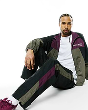 Mens Alder Nylon Colorblock Pant and matching relaxed-fit full-zip track jacket in black, olive green, and deep purple crinkled nylon, with a white Psycho Bunny chest logo.