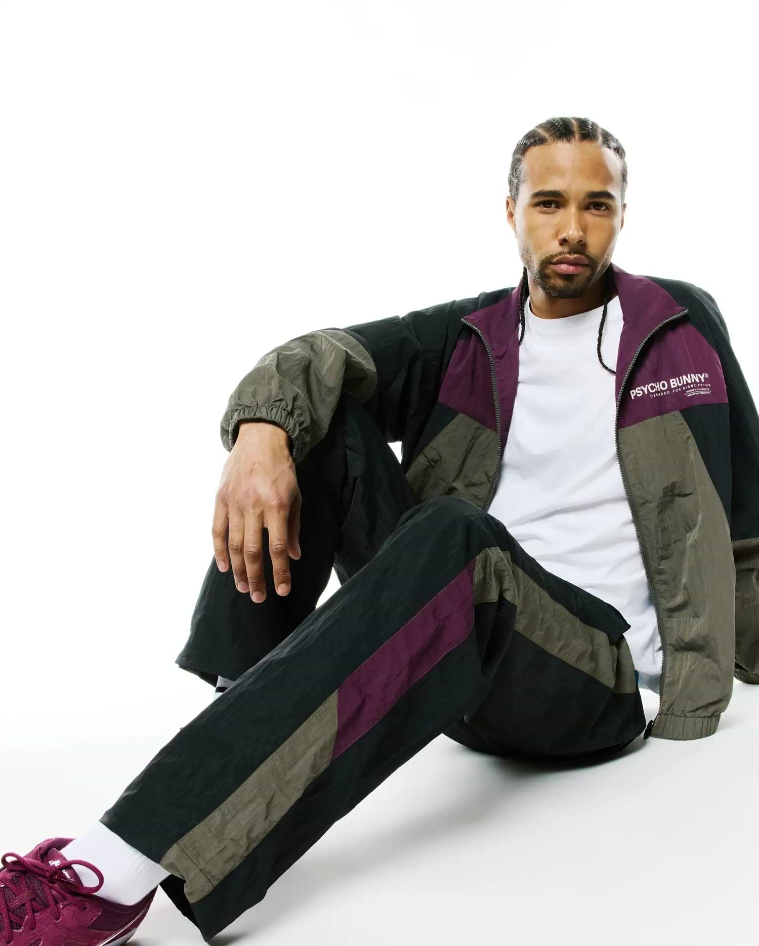 Mens Alder Nylon Colorblock Pant and matching relaxed-fit full-zip track jacket in black, olive green, and deep purple crinkled nylon, with a white Psycho Bunny chest logo.