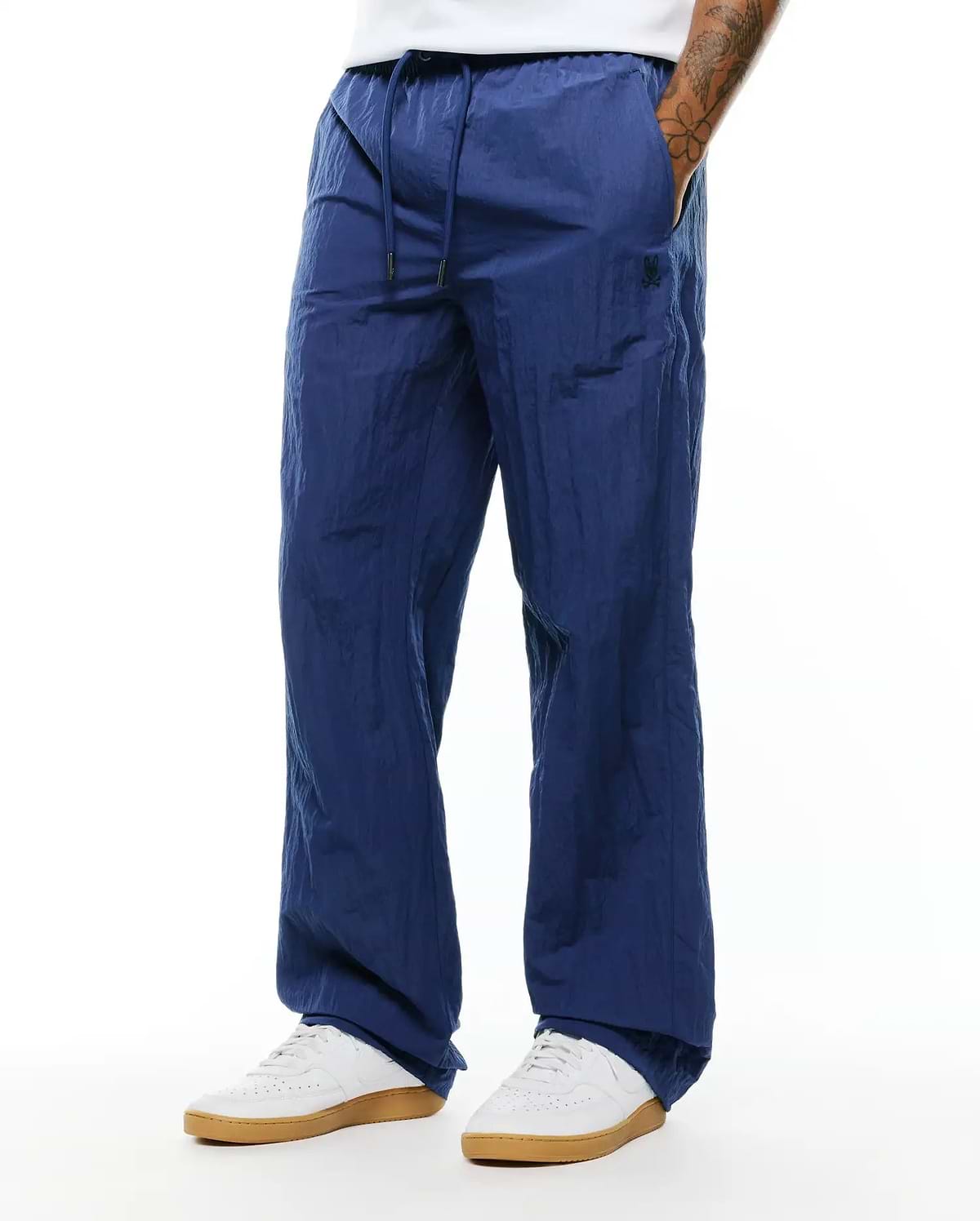 Mens Alder Nylon Pant in navy blue, featuring a relaxed fit, crinkled nylon texture, drawstring waist, and a small dark embroidered Psycho Bunny skull logo on the left thigh. (3)