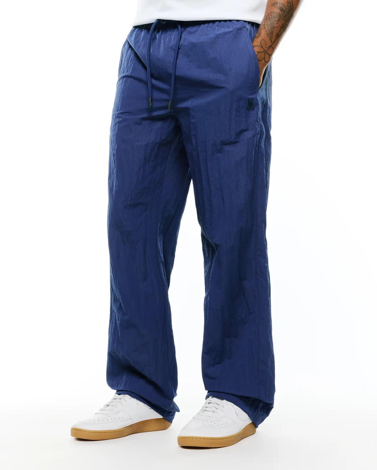 Mens Alder Nylon Pant in navy blue, featuring a relaxed fit, crinkled nylon texture, drawstring waist, and a small dark embroidered Psycho Bunny skull logo on the left thigh. (3)
