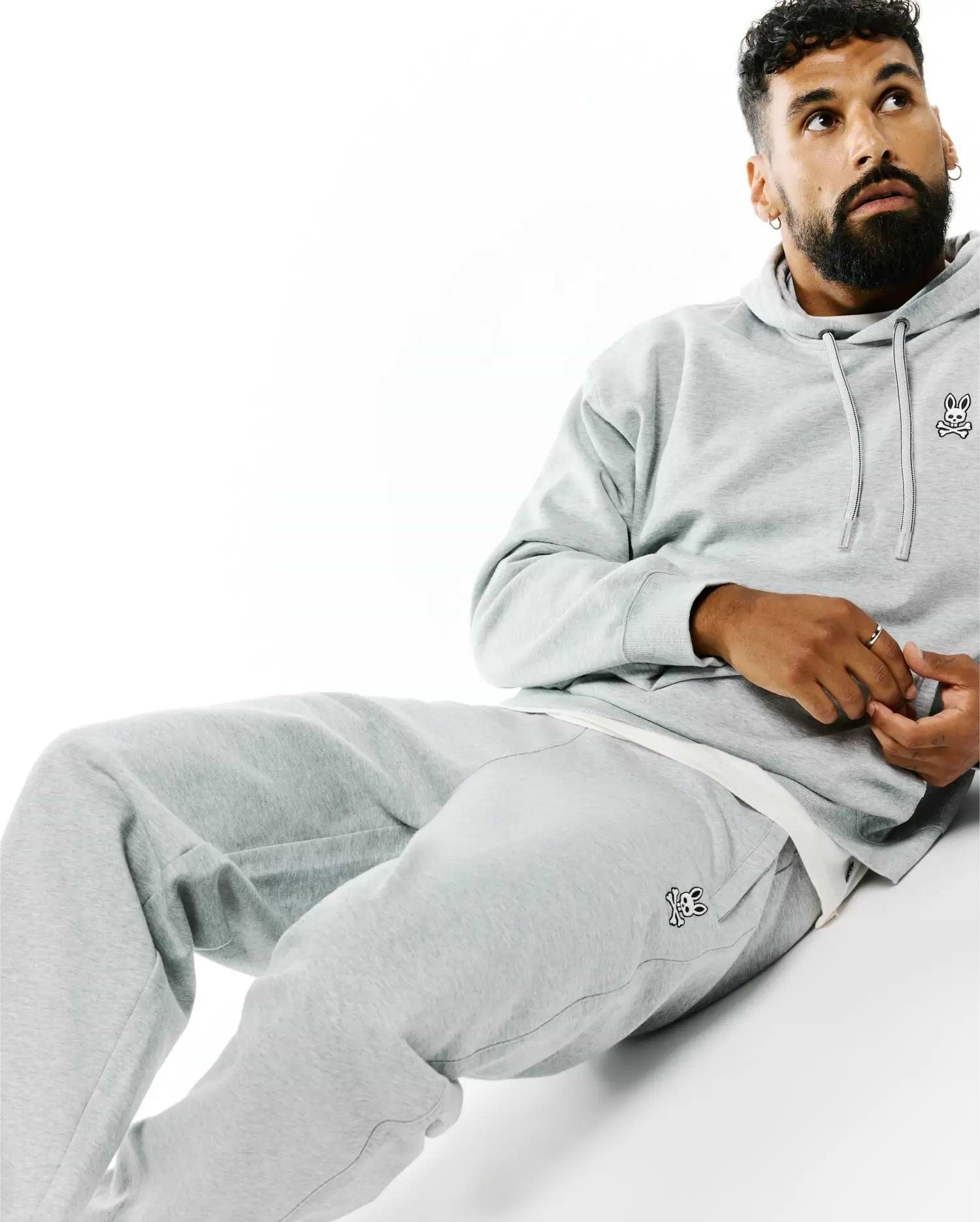 Grey relaxed fit brushed fleece hoodie with small embroidered Psycho Bunny skull logo on left chest, paired with matching Mens Terrence Brushed Fleece Sweatpant featuring the bunny skull logo on left thigh.