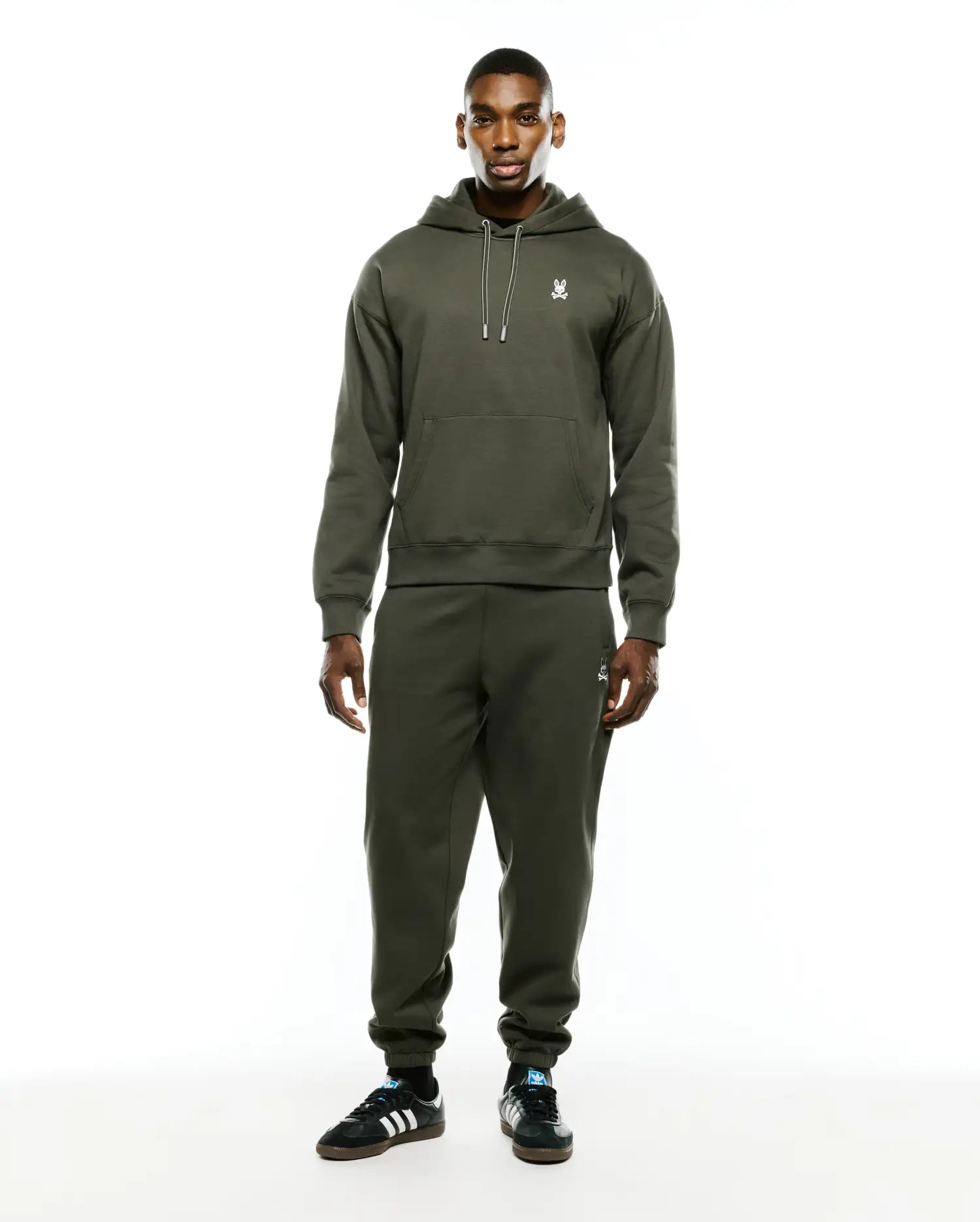 Olive green relaxed fit brushed fleece hoodie with white drawstring and embroidered Psycho Bunny skull chest logo. Paired with Mens Terrence Brushed Fleece Sweatpant, featuring an embroidered bunny skull thigh logo.