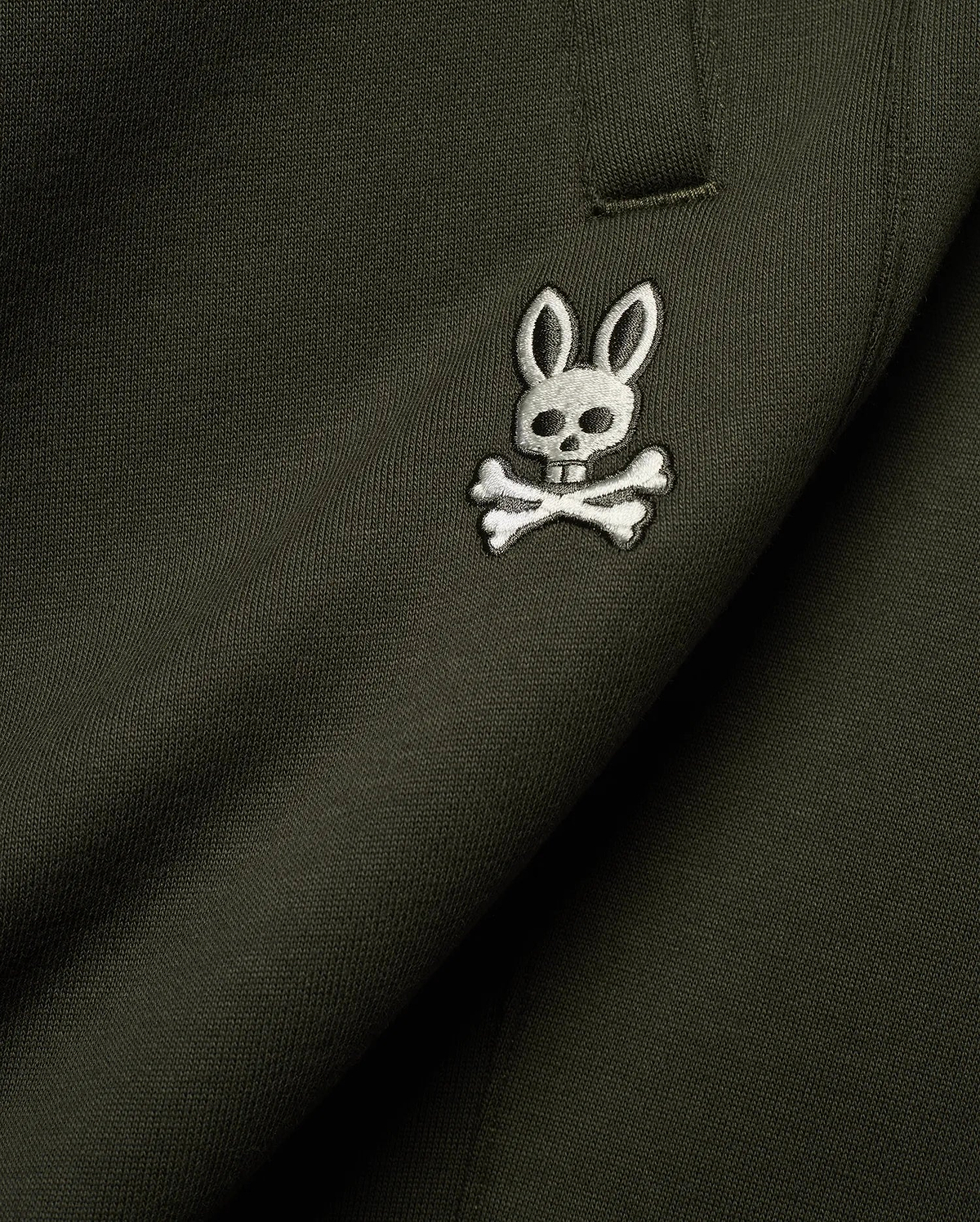 Mens Terrence Brushed Fleece Sweatpant in dark olive green, featuring a small, intricately embroidered white and silver Psycho Bunny skull logo on the upper leg, showcasing the soft brushed fleece knit texture.