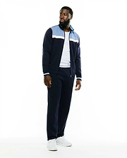 Navy blue Psycho Bunny track jacket and matching Men's Jacques Pique Track Pants. The jacket features light blue and white color-block panels, striped cuffs, and an embroidered white script logo on the chest. (1)