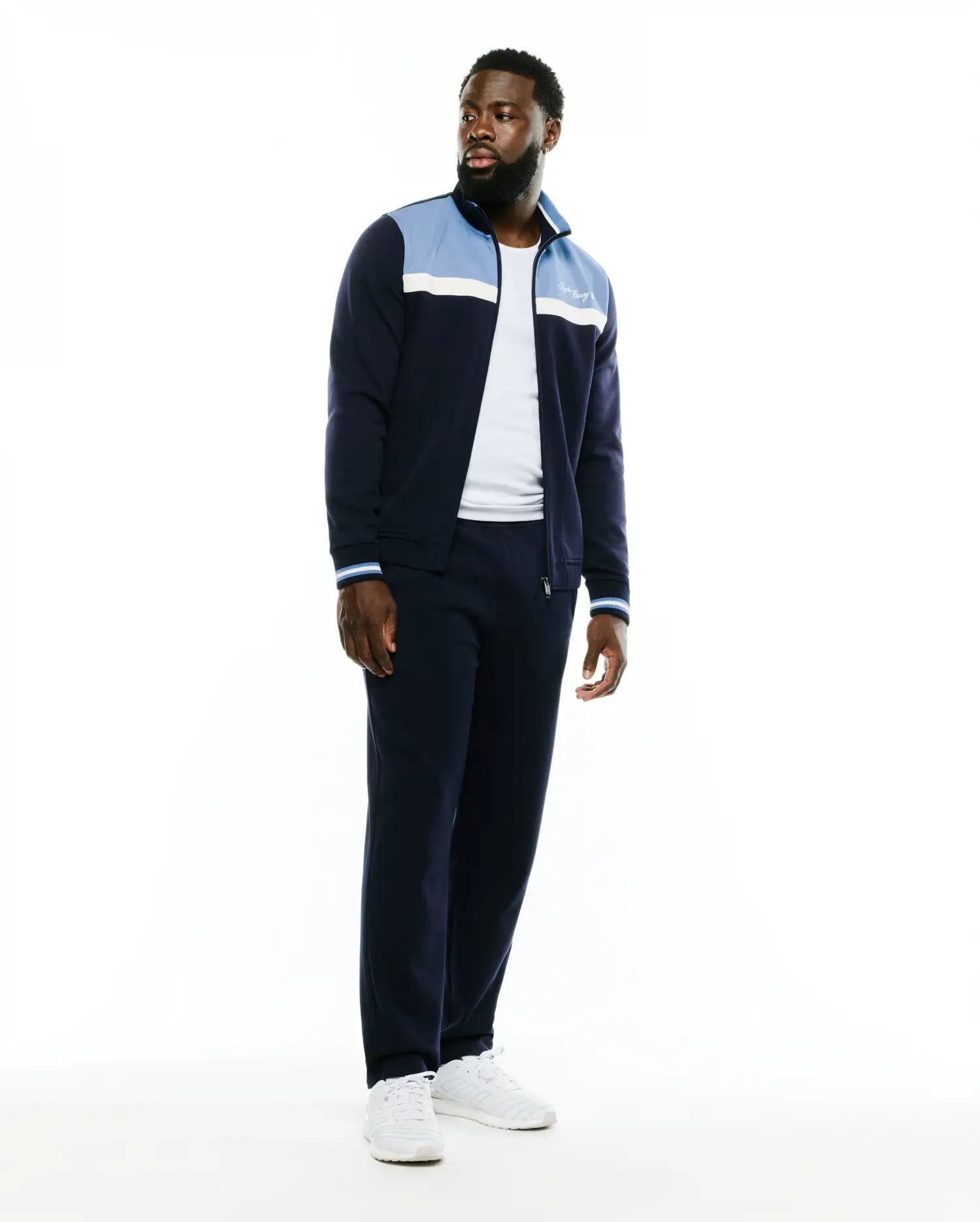 Navy blue Psycho Bunny track jacket and matching Men's Jacques Pique Track Pants. The jacket features light blue and white color-block panels, striped cuffs, and an embroidered white script logo on the chest. (1)