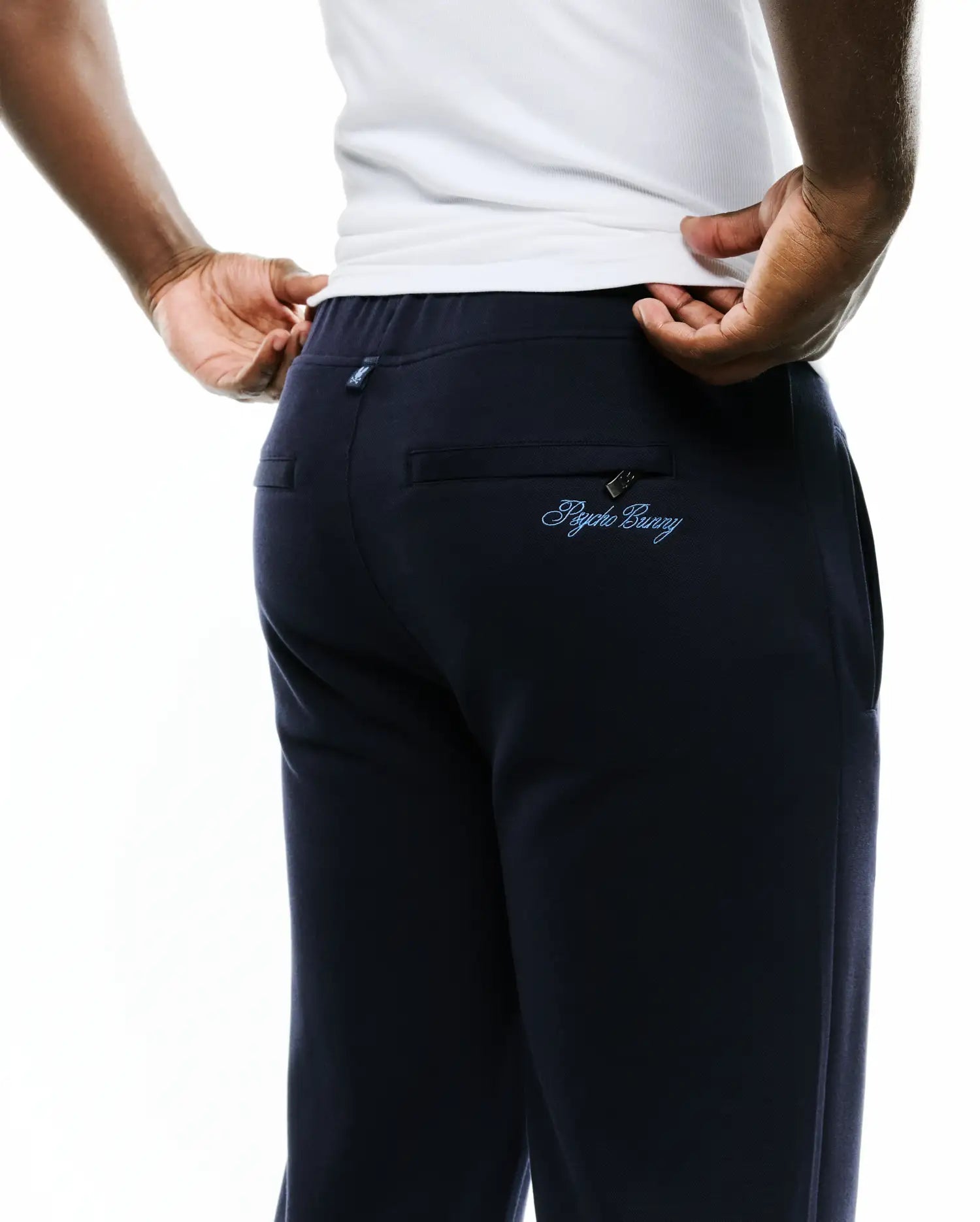 Men's Jacques Pique Track Pants in dark navy, featuring a relaxed fit, pique fabric, and a light blue embroidered Psycho Bunny script logo on the zippered back pocket, plus a small logo tag on the waistband. (3)
