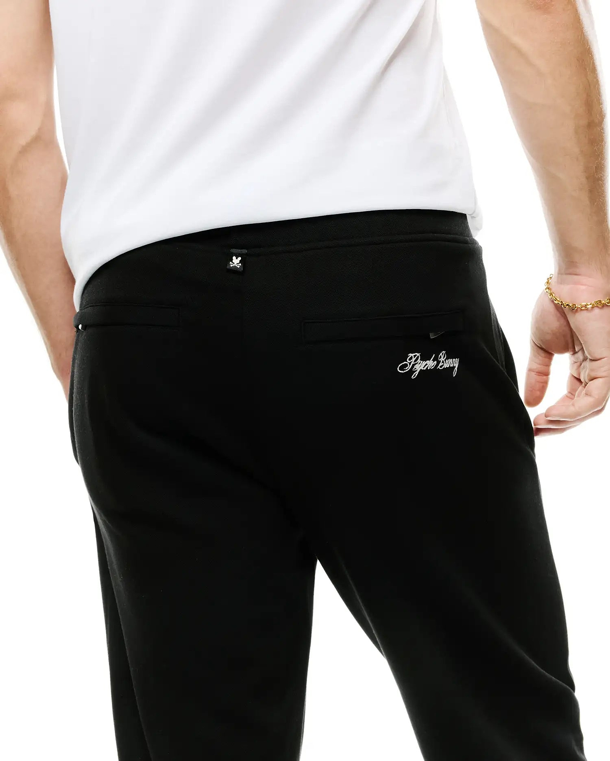Men's Jacques Pique Track Pants in black, featuring a subtle pique texture, relaxed fit, a small white Psycho Bunny skull logo tag on the waistband, and white embroidered Psycho Bunny script on the back right pocket. (3)