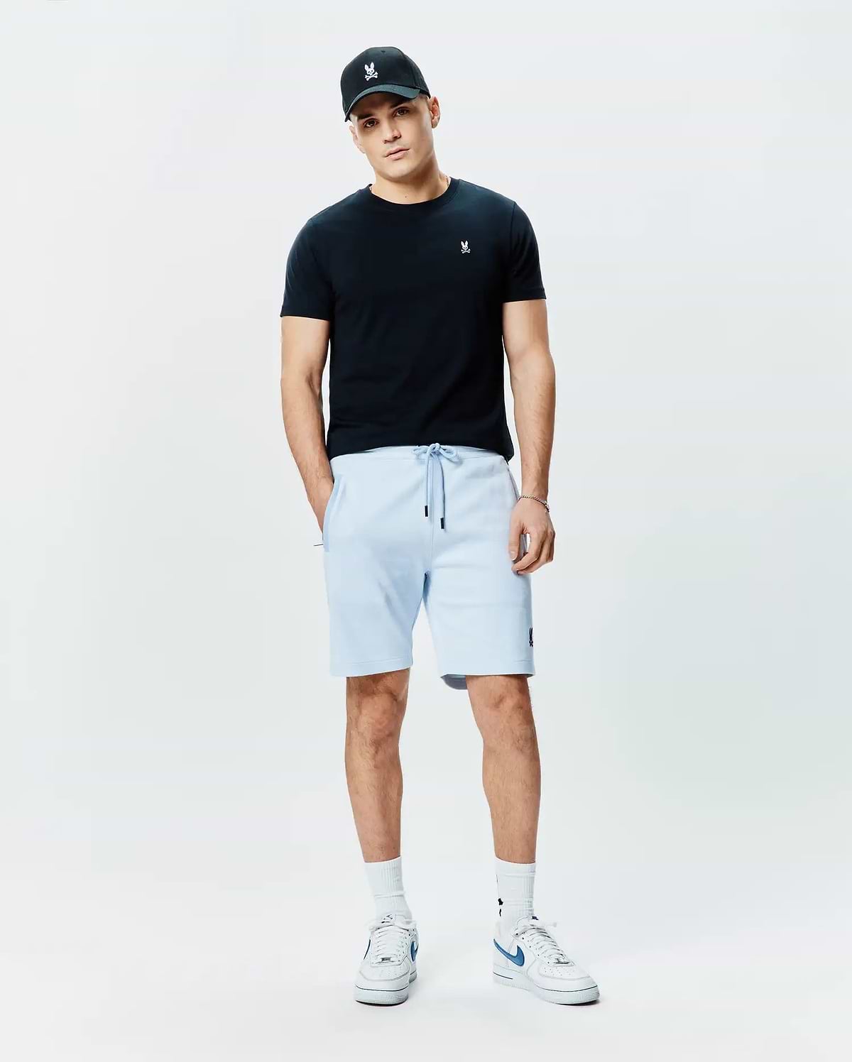 Black jersey t-shirt with white Psycho Bunny logo on chest, light blue Mens Keith Short 8 French terry shorts with black drawstrings and bunny logo on thigh, plus a black cap with white bunny skull.