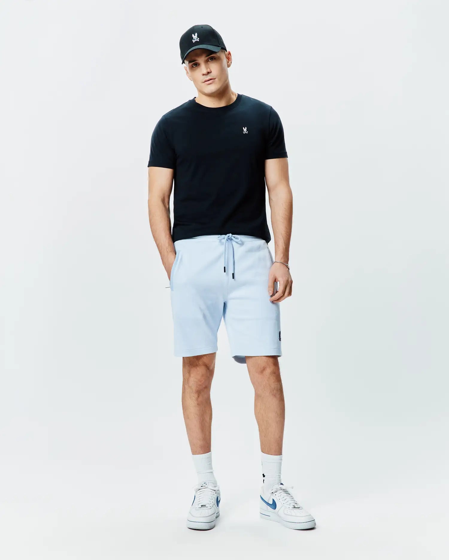 Black jersey t-shirt with white Psycho Bunny logo on chest, light blue Mens Keith Short 8 French terry shorts with black drawstrings and bunny logo on thigh, plus a black cap with white bunny skull.